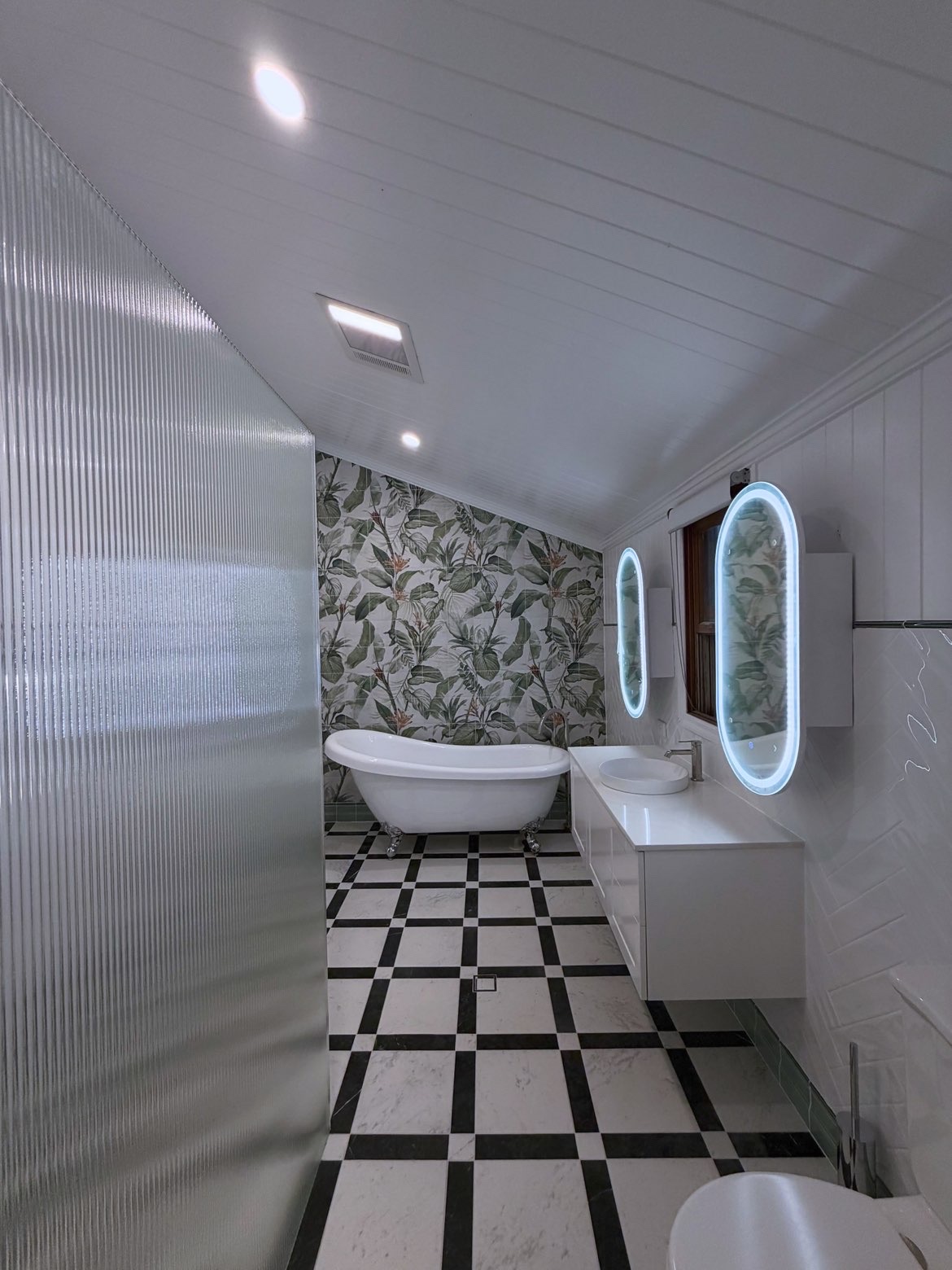 Bathroom renovation — freestanding tub, checkerboard floor, backlit oval mirrors
